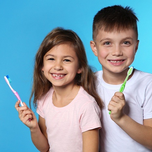 Two young children with dental sealants smiling and holding toothbrushes